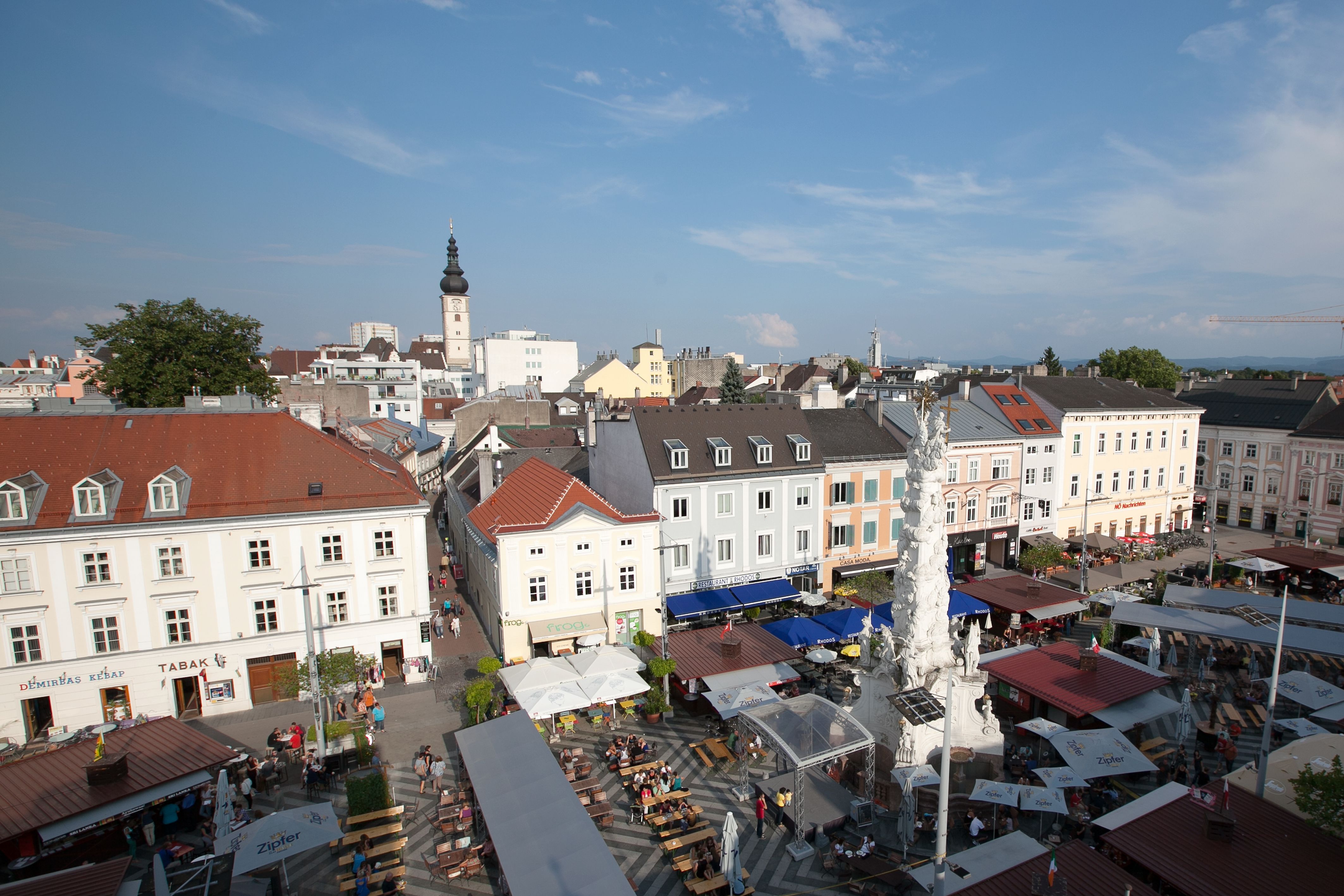 Luftaufnahme eines belebten Platzes in St. Pölten mit Marktständen und einem Turm im Hintergrund.