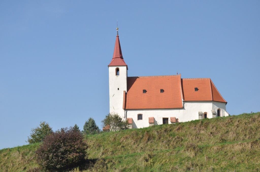 Pfarrkirche Ofenbach auf einem Hügel mit blauem Himmel im Hintergrund.
