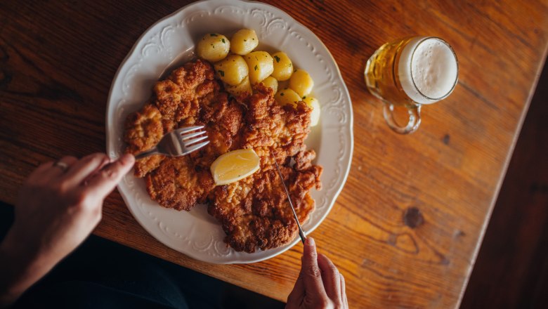 Teller mit Schnitzel, Kartoffeln und Zitrone, daneben ein Glas Bier.