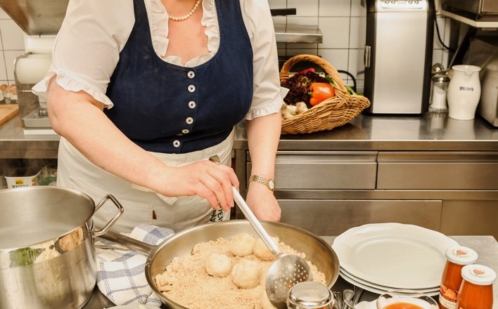Frau in traditioneller Kleidung kocht in einer K&uuml;che mit regionalen Zutaten.