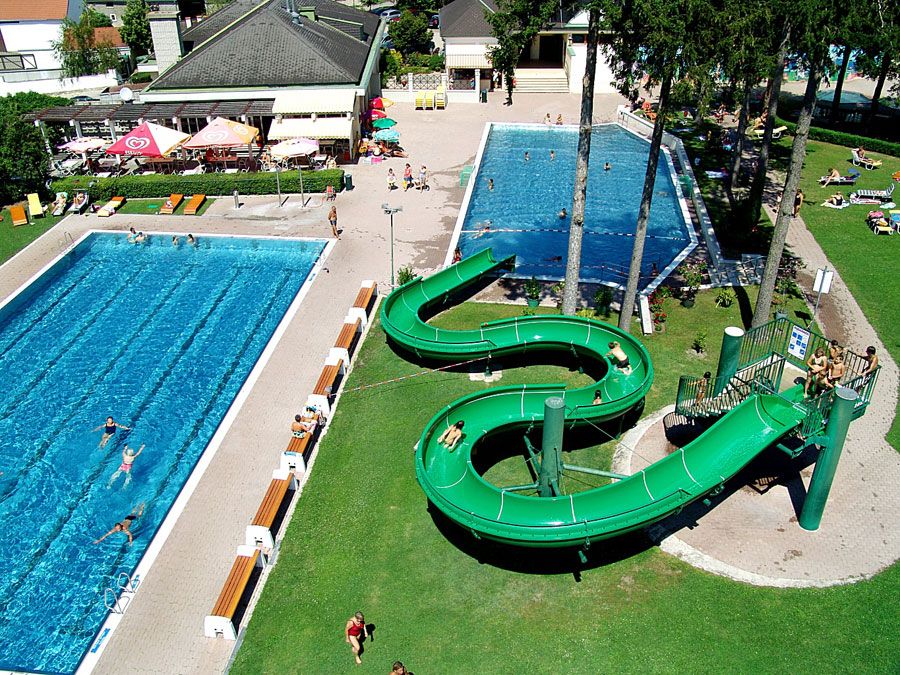 Luftaufnahme eines Freibads mit zwei Becken und einer grünen Wasserrutsche.