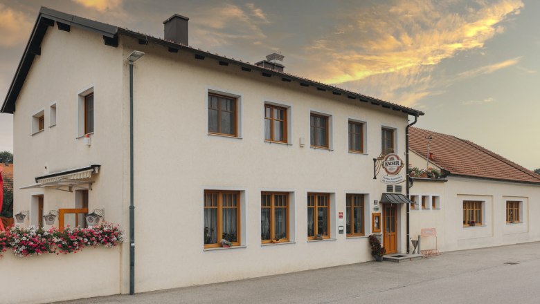 Gasthaus mit Blumenschmuck und Kaiser-Bierschild bei Sonnenuntergang.
