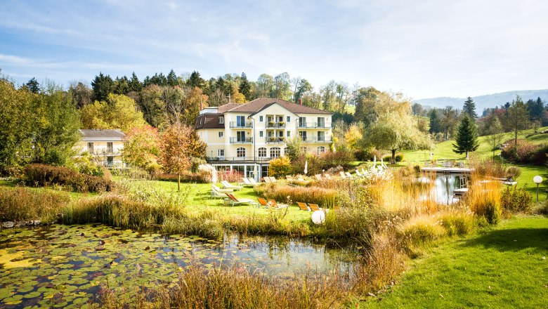RelaxResort Kothmühle, © Johanna Meinschad Ein Hotel inmitten einer grünen Landschaft mit Teich und Liegestühlen.