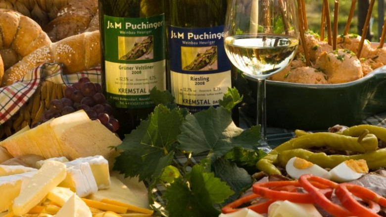 Heurigenjause mit Wein, K&auml;se, Brot und Aufschnitt auf einem Tisch.