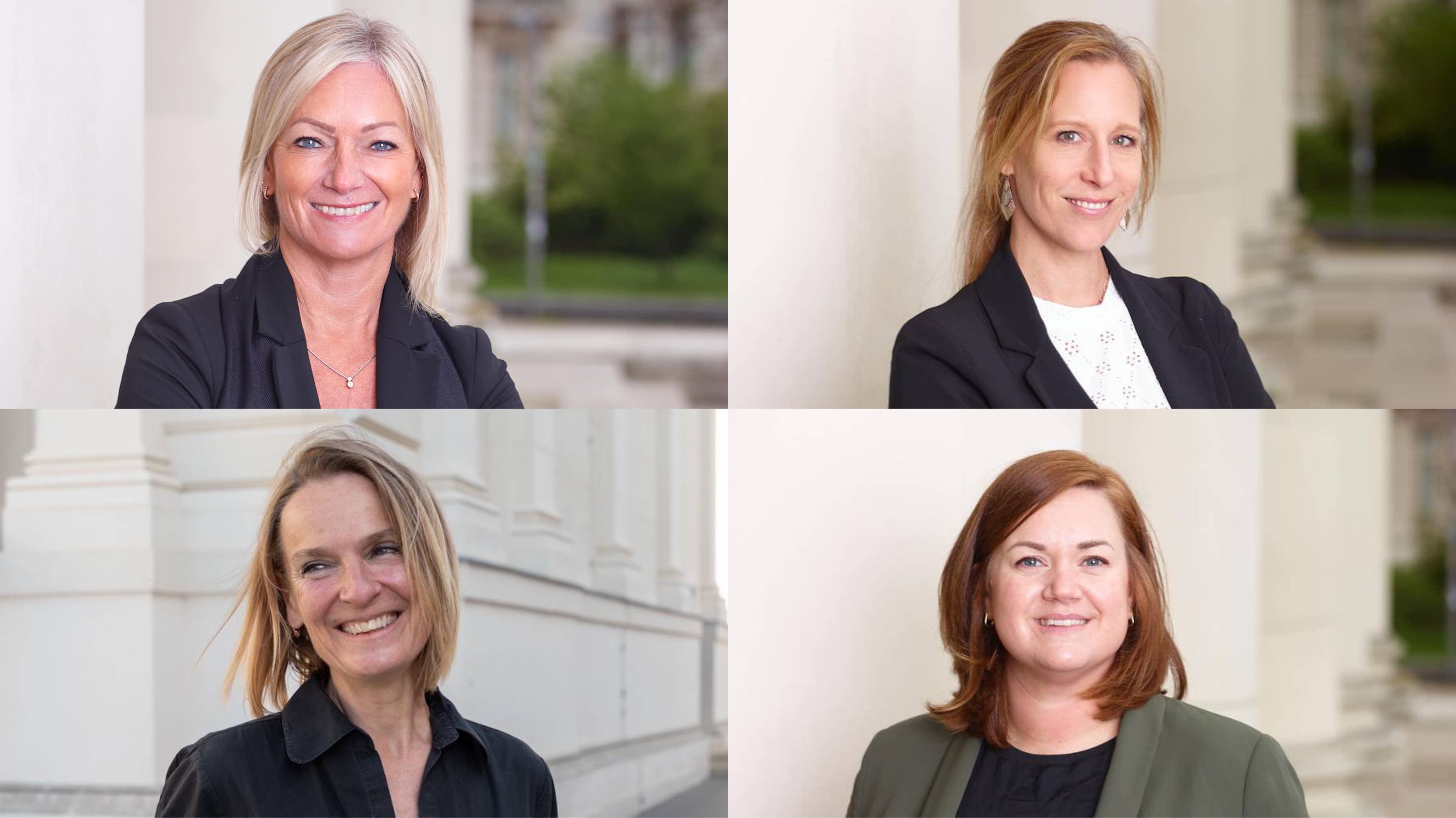 Vier Frauen in Business-Kleidung lächeln in die Kamera, vor einem Gebäude mit Säulen.