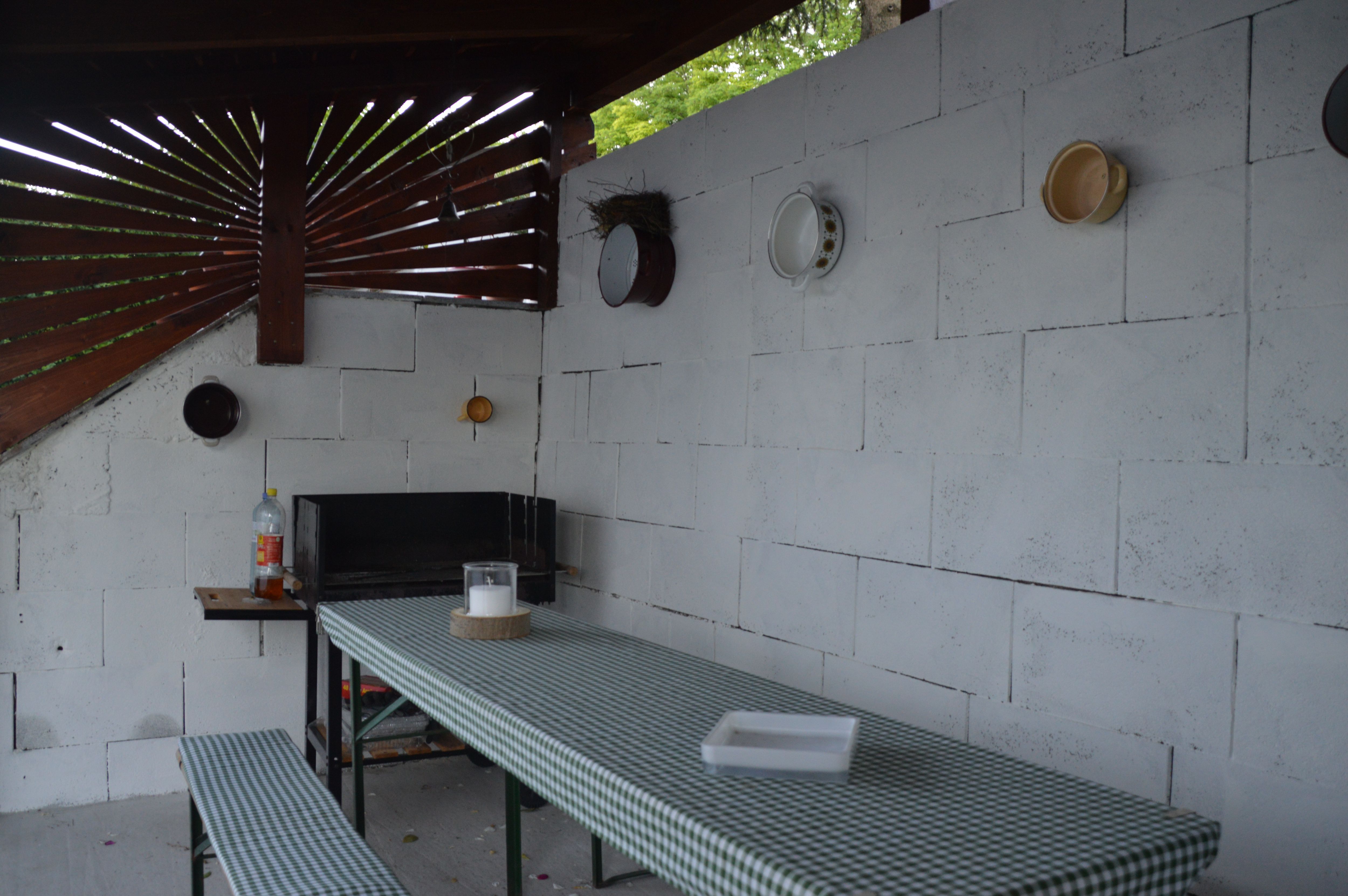 Überdachter Grillplatz mit Tisch und Bänken, dekoriert mit Geschirr an der Wand.
