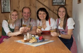 Eine Familie in traditioneller Kleidung stößt mit Weingläsern an einem Holztisch an.