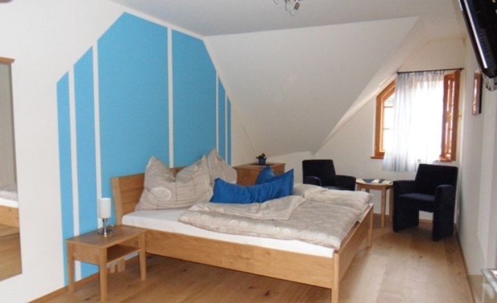 Ein Schlafzimmer mit blau-weißer Wand, Holzbett, zwei Sesseln und einem Fenster mit Vorhang.