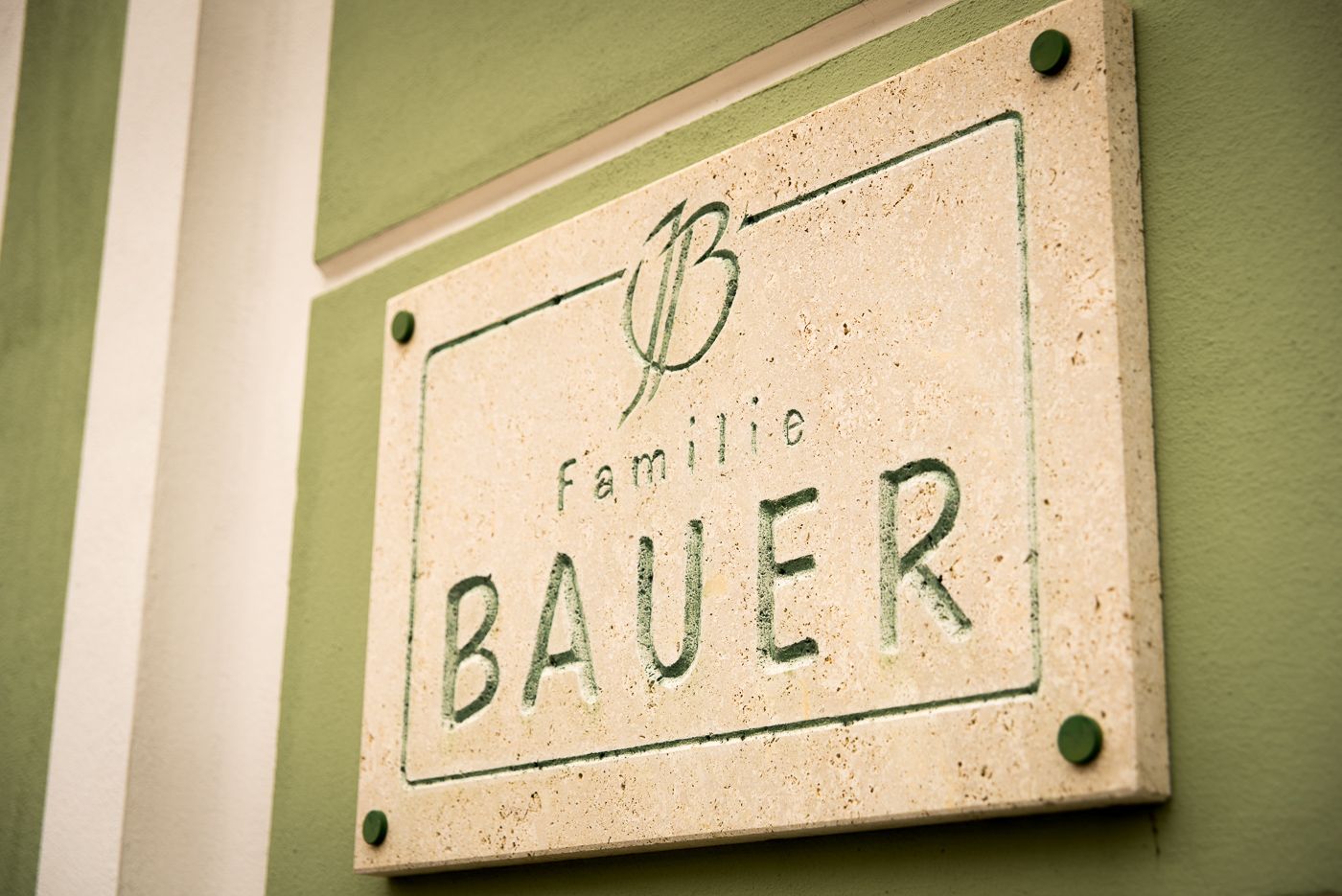 Steintafel mit der Aufschrift 'Familie Bauer' an einer grünen Wand.