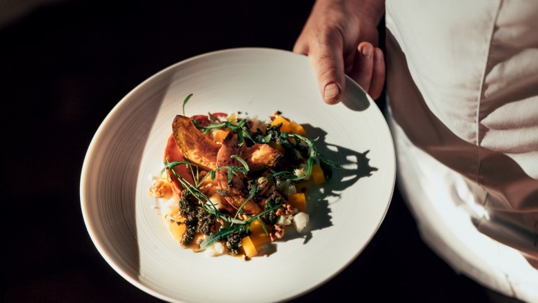 Ein Teller mit einem kunstvoll angerichteten Gericht wird von einer Person in wei&szlig;er Kleidung gehalten.