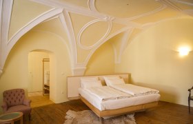 Ein elegantes Schlafzimmer mit gew&ouml;lbter Decke, einem Doppelbett, einem Sessel und Holzboden.