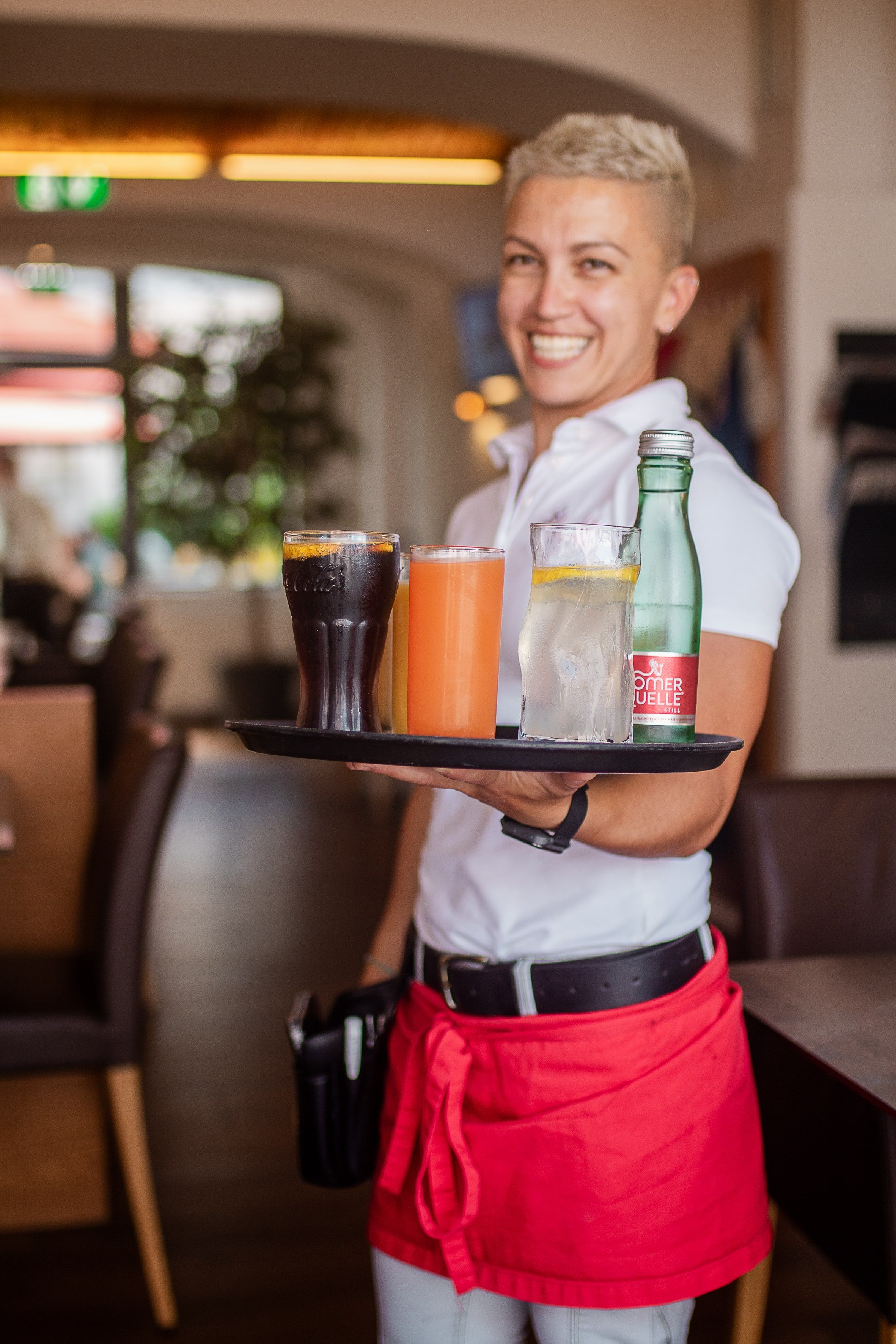 Eine lächelnde Kellnerin in einem Restaurant trägt ein Tablett mit verschiedenen Getränken.