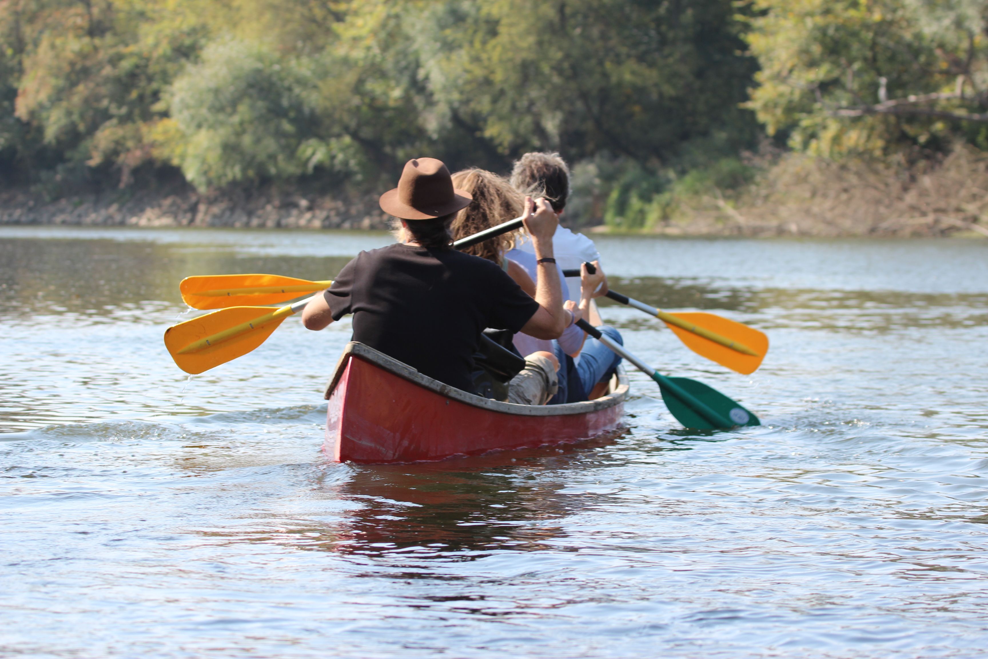 Drei Personen paddeln in einem roten Kanu auf einem Fluss.