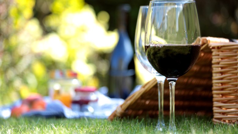 Zwei Weingläser und ein Picknickkorb auf einer Wiese.