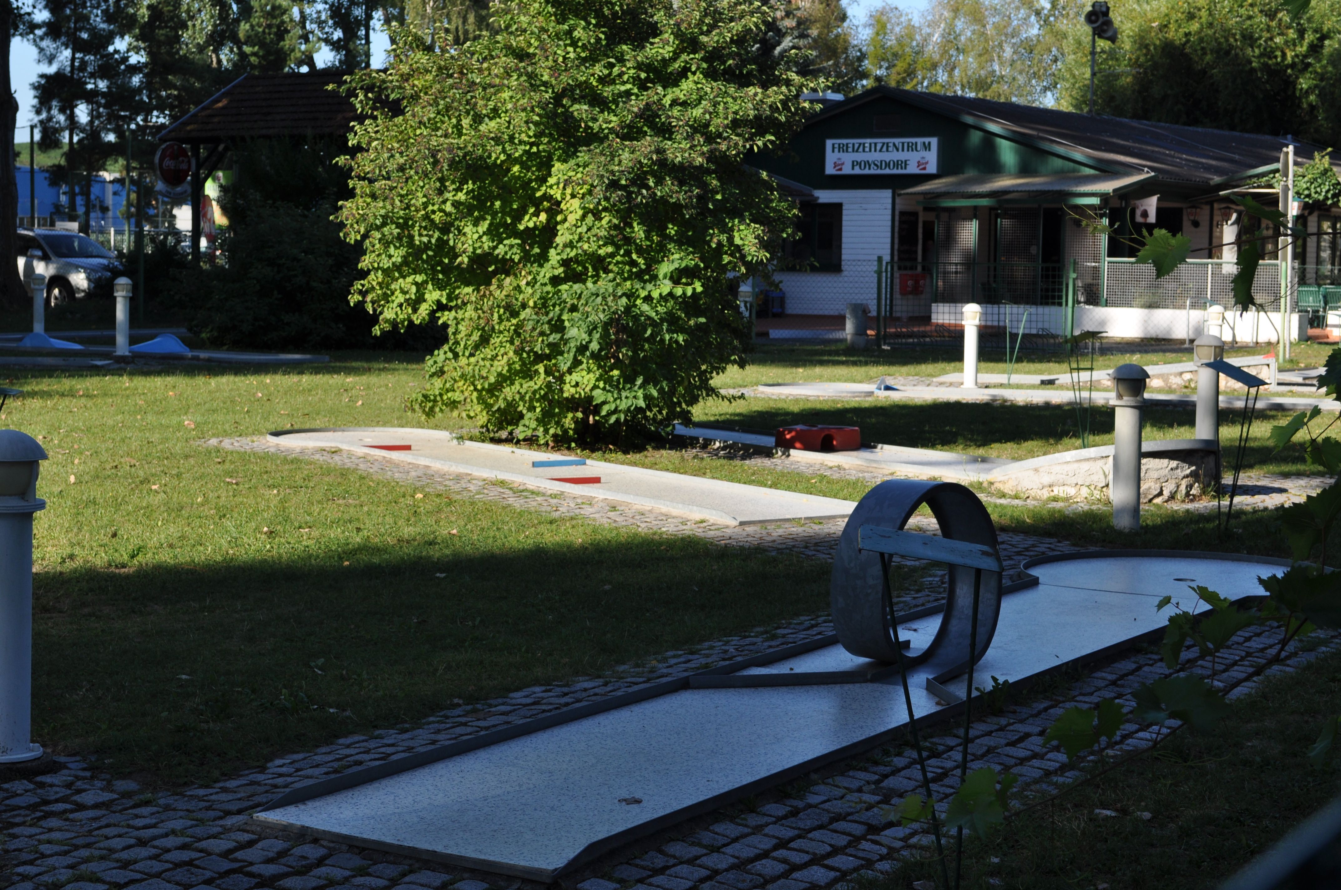 Minigolfplatz mit Hindernissen und einem Gebäude im Hintergrund.