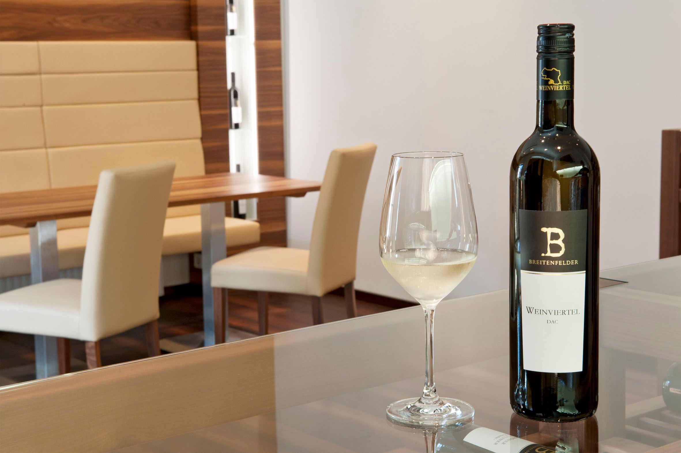 Ein Verkostungsraum mit einer Flasche Weißwein und einem gefüllten Weinglas auf einem Tisch.