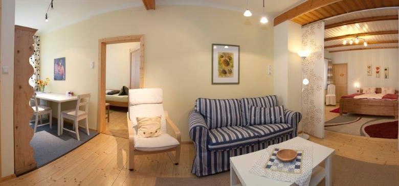 Panorama eines gemütlichen Wohnzimmers mit Sofa, Esstisch und Schlafzimmer im Hintergrund.