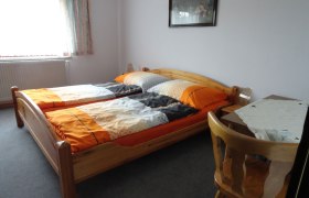 Ein einfach eingerichtetes Schlafzimmer mit zwei Einzelbetten, einem Tisch und einem Stuhl.