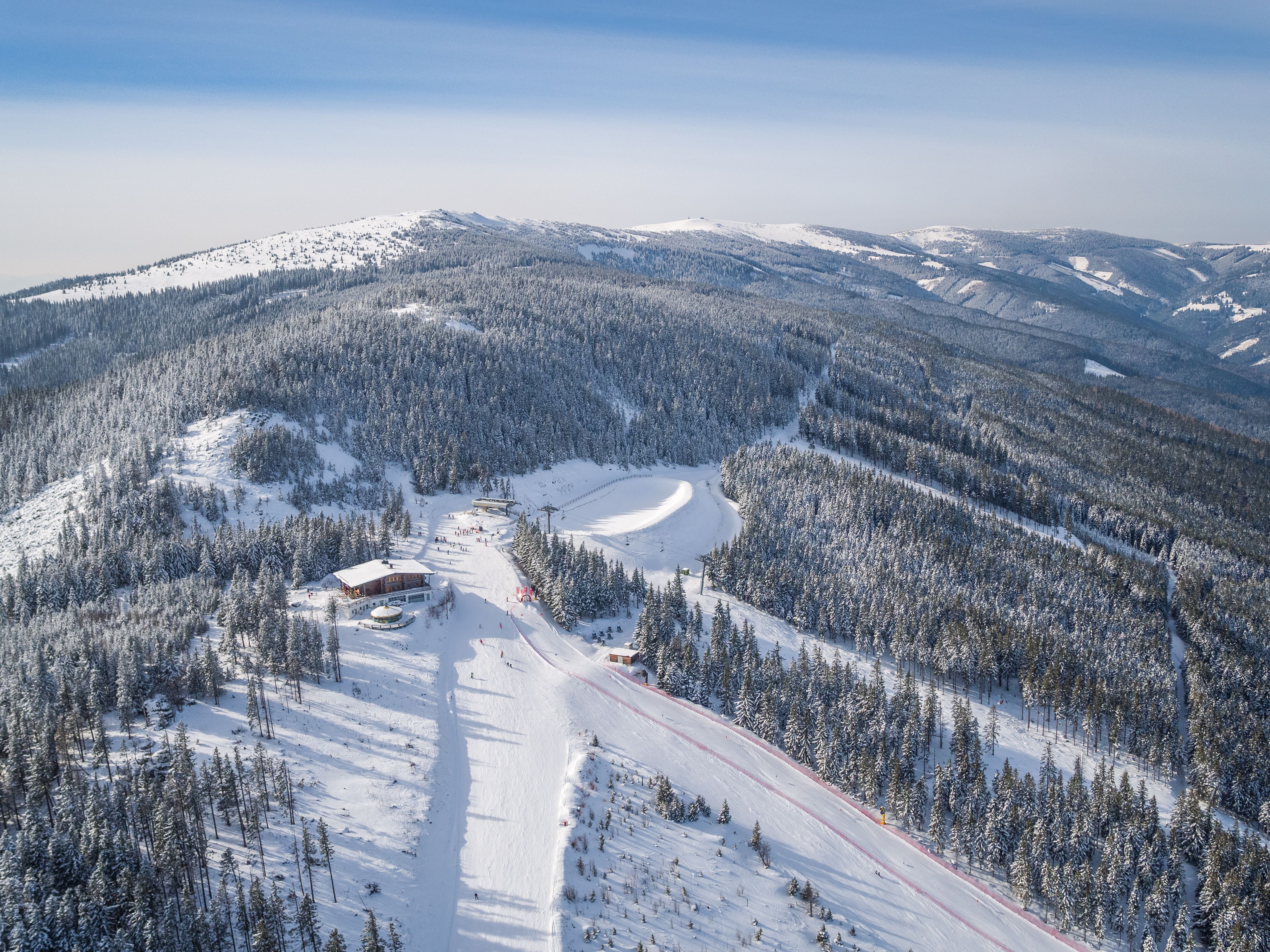 Skigebiet mit Sessellift und Skifahrern, umgeben von schneebedeckten Bäumen und Hügeln.