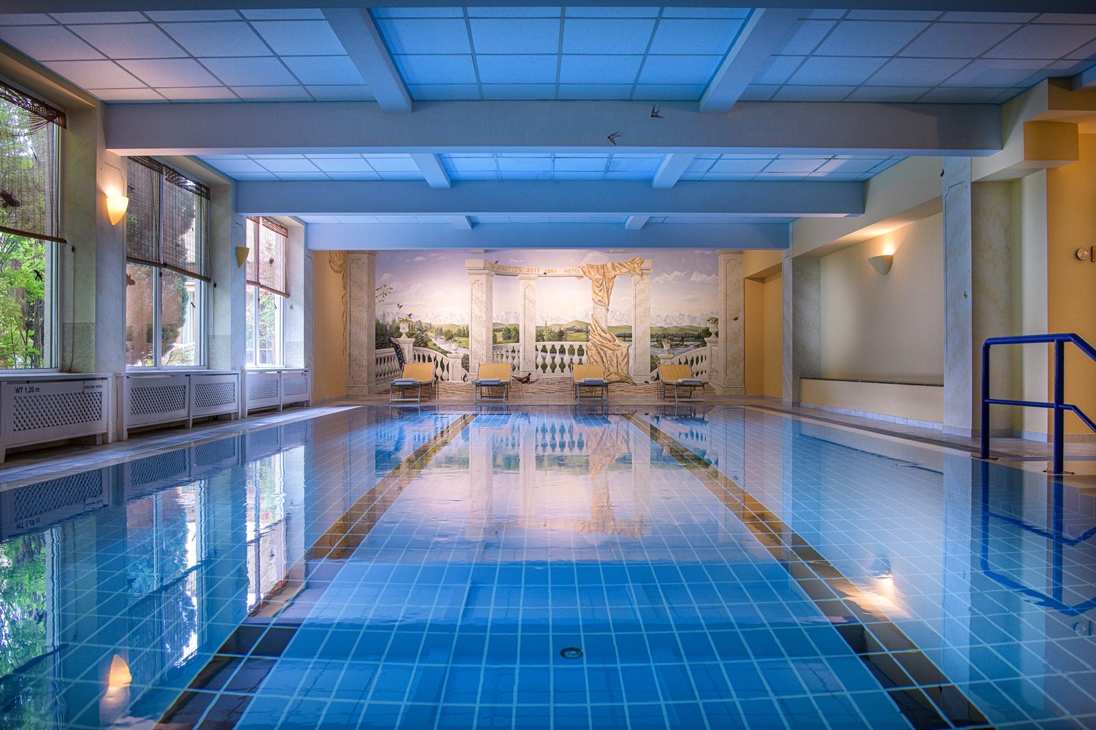 Innenansicht eines Hallenbads mit blauem Wasser und Wandgemälde.