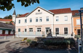 Ein Gebäude mit der Aufschrift 'Bärenhof' und 'bed - breakfast' in einer sonnigen Umgebung mit einem Brunnen im Vordergrund.