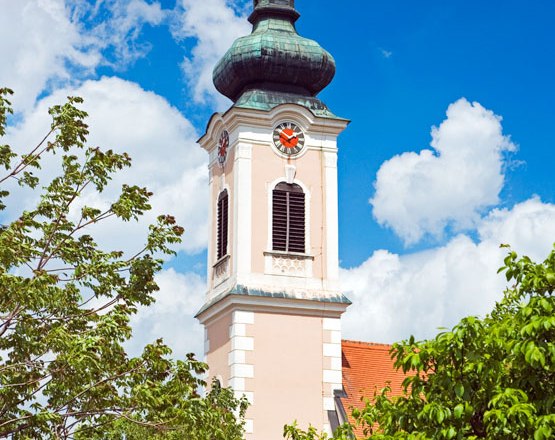 Turm einer Kirche mit Uhr und grünem Dach vor blauem Himmel.