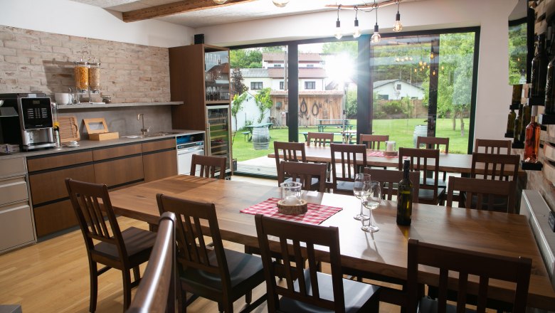 Esszimmer mit Holztisch, St&uuml;hlen und Blick auf den Garten durch gro&szlig;e Fenster.