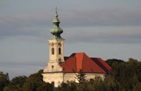 Pfarrkirche St. Nikolaus in Wolfpassing mit rotem Dach und grünem Turm vor bewölktem Himmel.