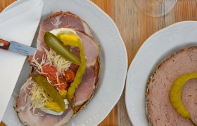 Zwei Teller mit belegten Broten und zwei Gl&auml;ser Wei&szlig;wein auf einem Holztisch.