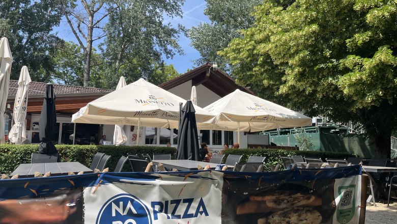 Gastgarten mit Blick auf das Geb&auml;ude der Pizzeria, im Hintergrund B&auml;ume.