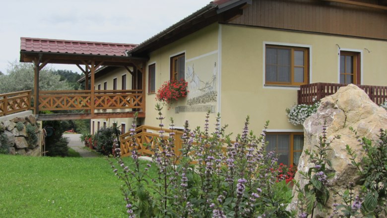 Steinbauer, © Fam. König Ein gelbes Gebäude mit Holzbalkon und Blumen, umgeben von grüner Landschaft.