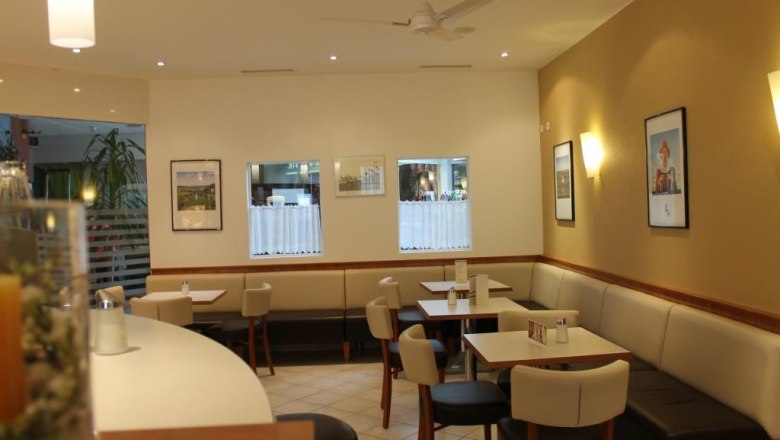 Innenansicht eines Caf&eacute;s mit Tischen, St&uuml;hlen und Wanddekorationen.