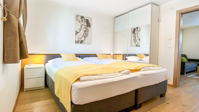 Modernes Schlafzimmer mit Doppelbett, gelber Bettdecke und gro&szlig;em Kleiderschrank mit Spiegeln.