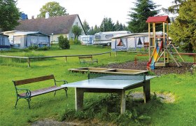 Campingplatz mit Tischtennisplatte, Spielplatz und Wohnwagen.
