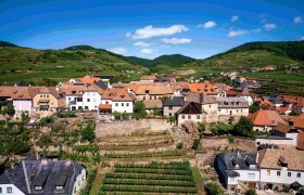 Ansicht von Wei&szlig;enkirchen mit dem Ortsteil Burg mit zahlreichen H&auml;usern, einem Weing&auml;rten und H&uuml;geln im Hintergrund