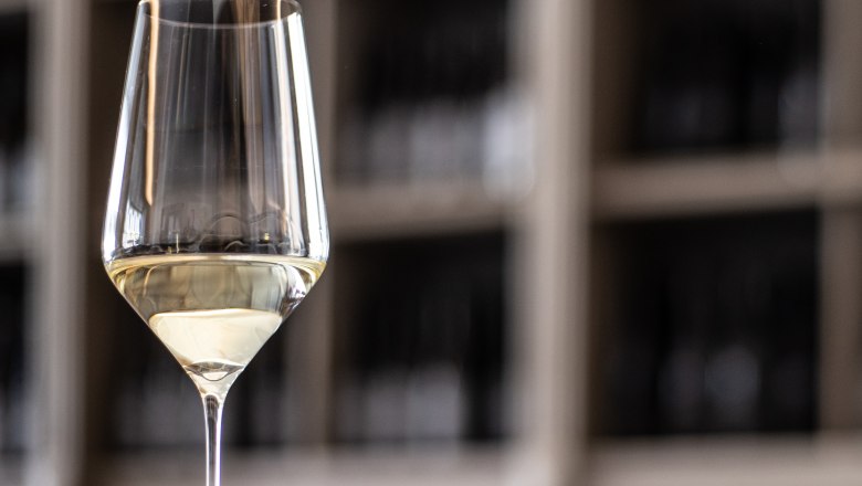 Nahaufnahme eines Weinglases mit Wei&szlig;wein vor einem unscharfen Hintergrund.