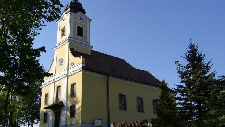 Pfarrkirche Haugschlag mit gelber Fassade und Turm, umgeben von B&auml;umen.