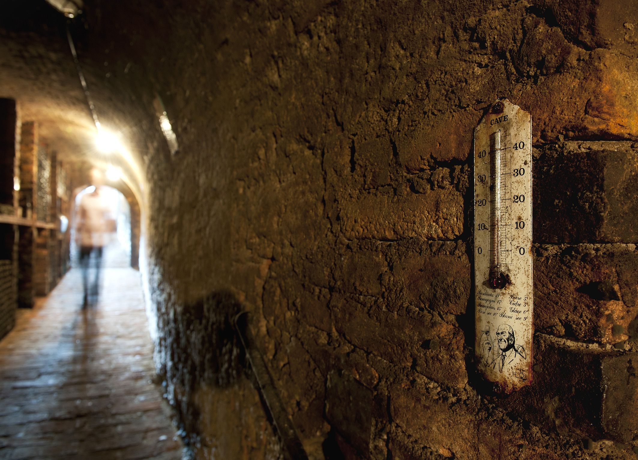 Ein alter Weinkeller mit einem Thermometer an der Wand und einer unscharfen Person im Hintergrund.