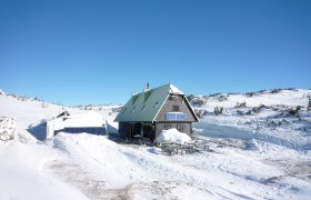 Eine Bergh&uuml;tte im Schnee mit Solarpanelen und blauem Himmel.