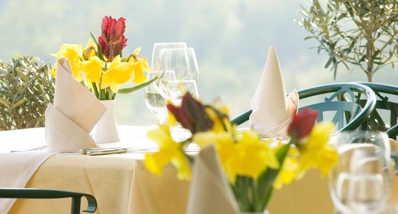 Ein elegant gedeckter Tisch im Freien mit gelben und roten Blumen, wei&szlig;en Servietten und Weingl&auml;sern.