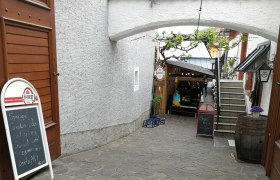 Eingang zu einem gemütlichen Innenhof mit Tischen und Pflanzen.