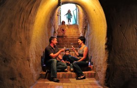 Familie sitzt in einem Weinkeller auf Treppen und trinkt Wein.