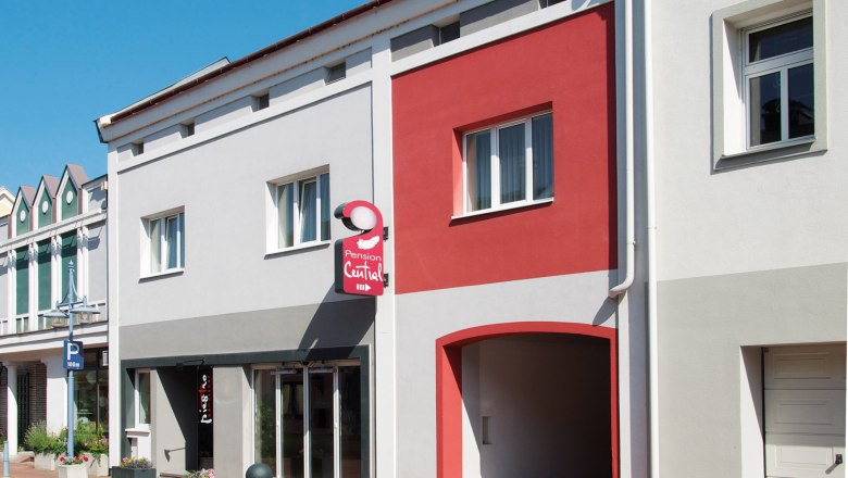 Pension Central, © dh Fassade der Pension Central mit grauen und roten Wänden, einem Schild und Fenstern.