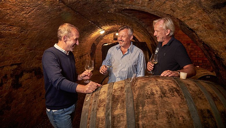 Drei Männer in einem Weinkeller, die Wein probieren.