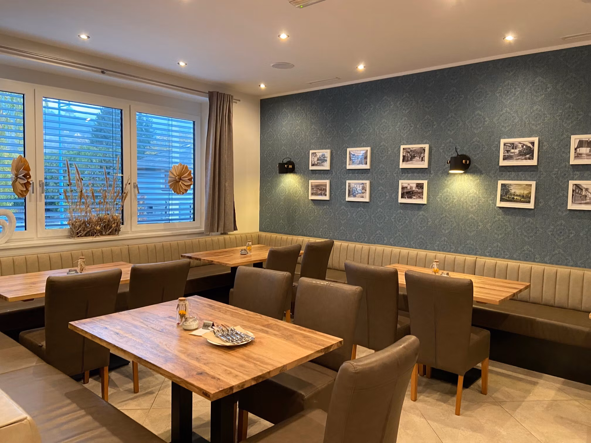 Innenansicht eines Restaurants mit Holztischen, gepolsterten Stühlen und einer Wand mit gerahmten Bildern.