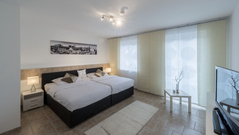 Modern eingerichtetes Schlafzimmer mit zwei Betten, Nachttischen, einem Bild an der Wand und einem Fernseher.