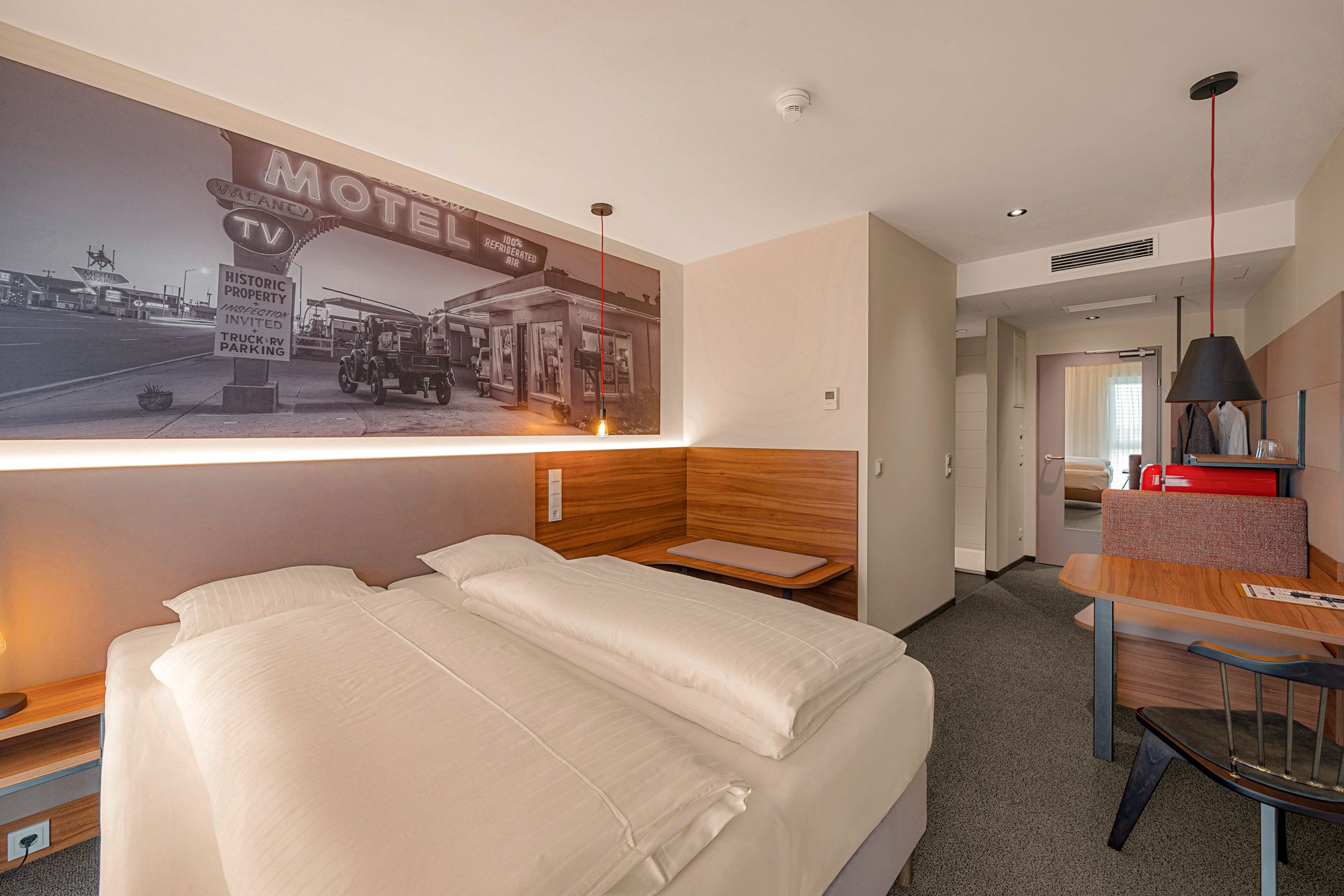 Modernes Hotelzimmer mit Doppelbett, Wandbild eines alten Motels, Holzmöbeln und Schreibtisch.