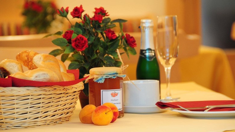Fr&uuml;hst&uuml;ckstisch mit Br&ouml;tchenkorb, Marmelade, Sektflasche und Rosen.