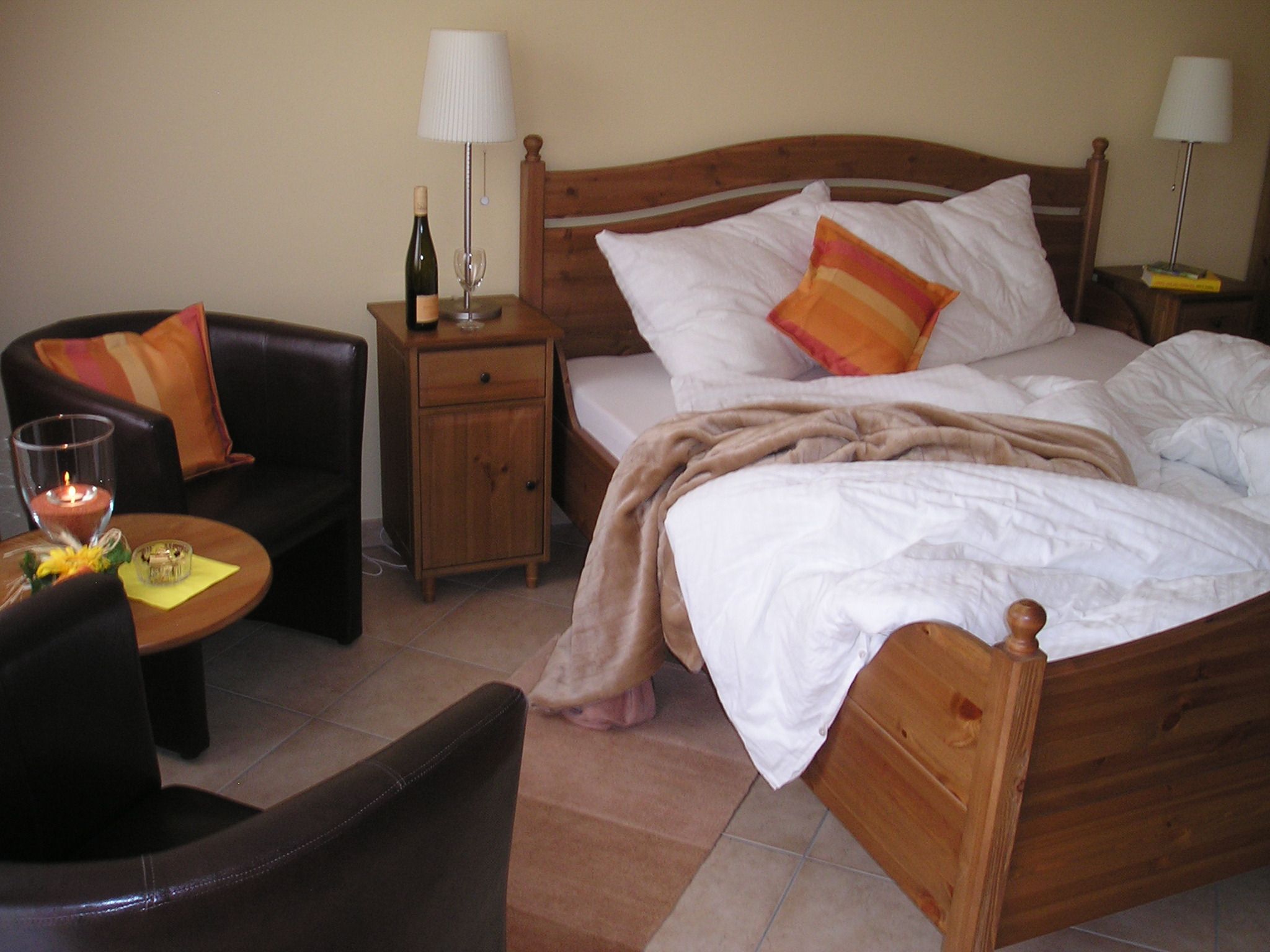 Gemütliches Gästezimmer mit Doppelbett, Nachttisch, Lampe, Sessel und Tisch.