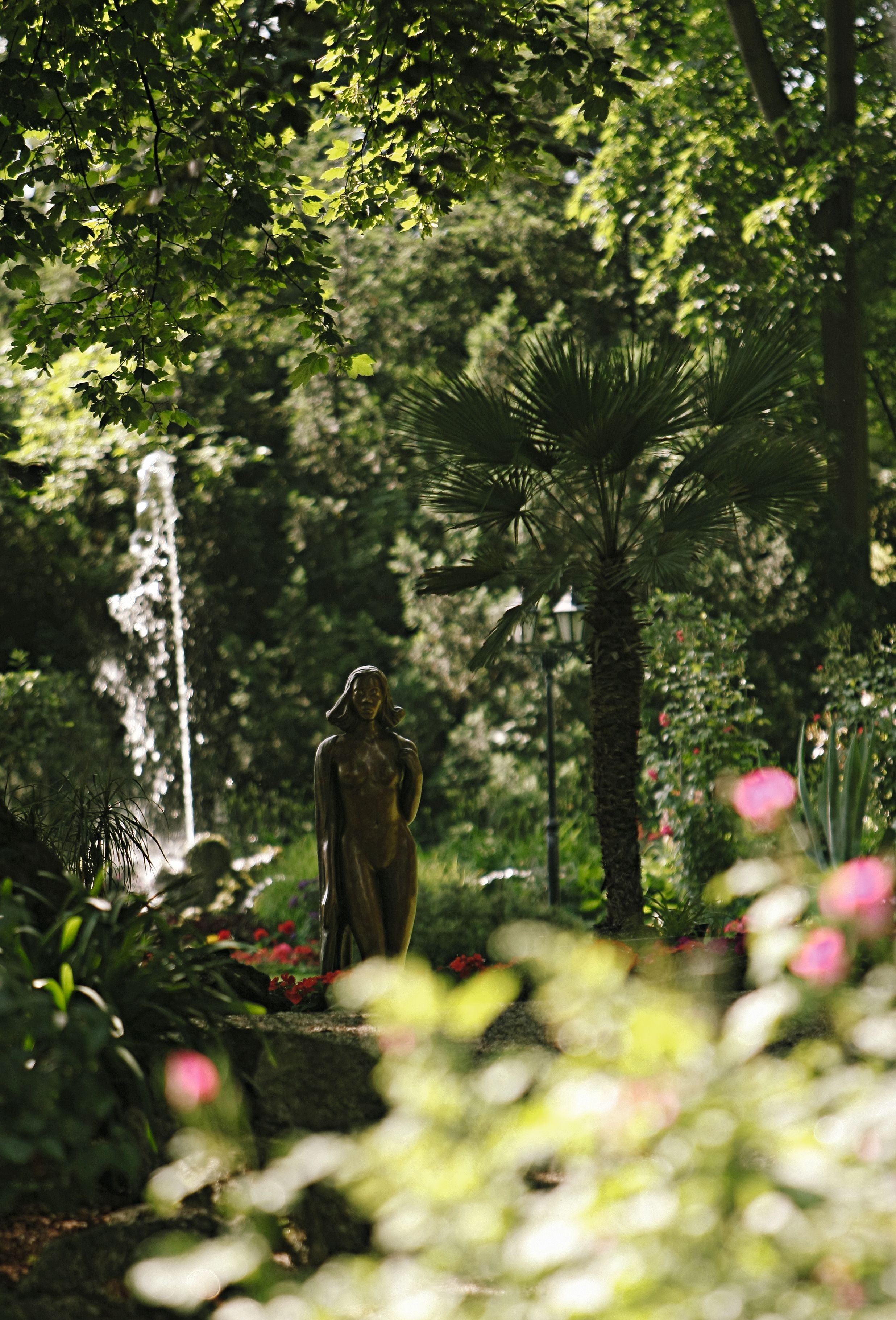 Eine Statue in einem grünen Garten mit einem Springbrunnen im Hintergrund.